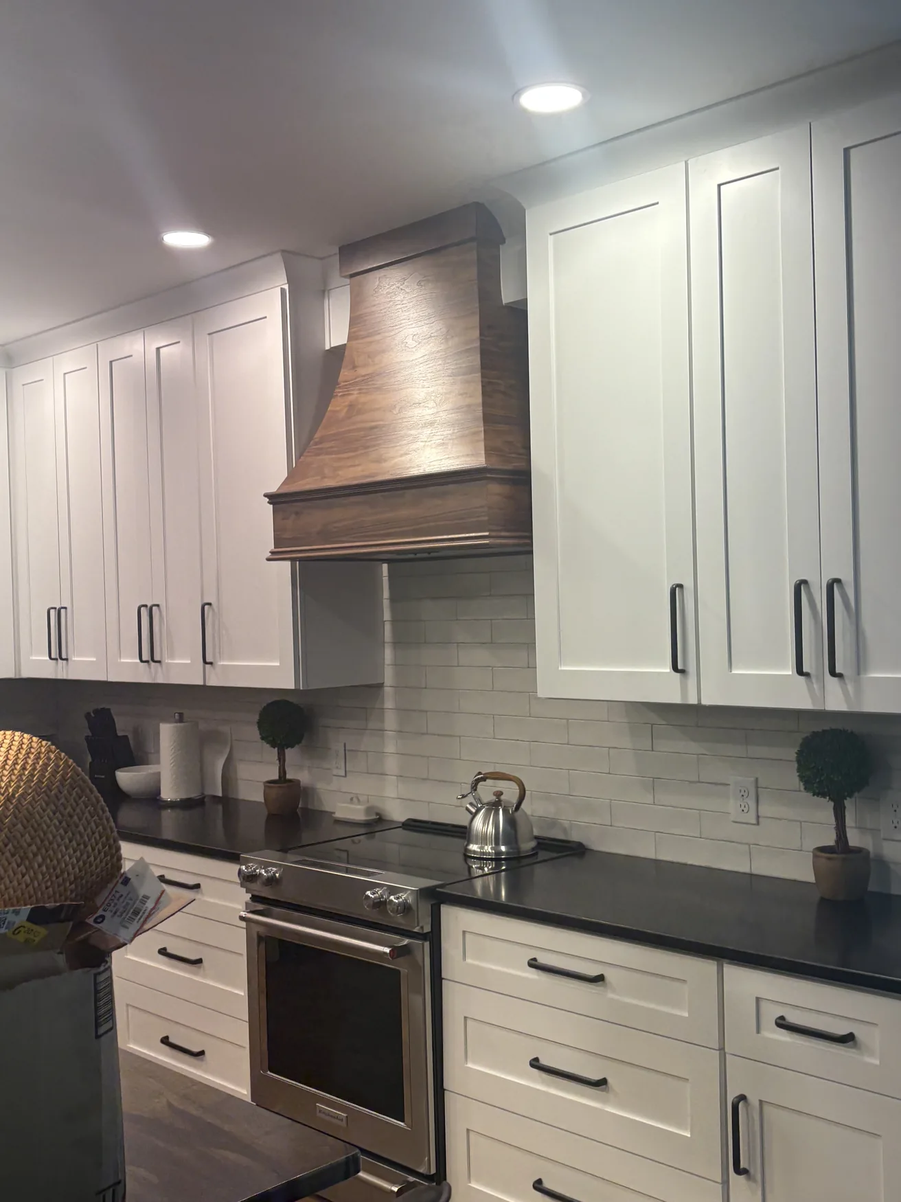 White kitchen cabinetry, dark countertops and a fitted wood range hood